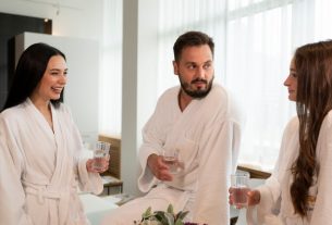 Three adults enjoying a relaxing spa day, chatting and drinking water indoors.
